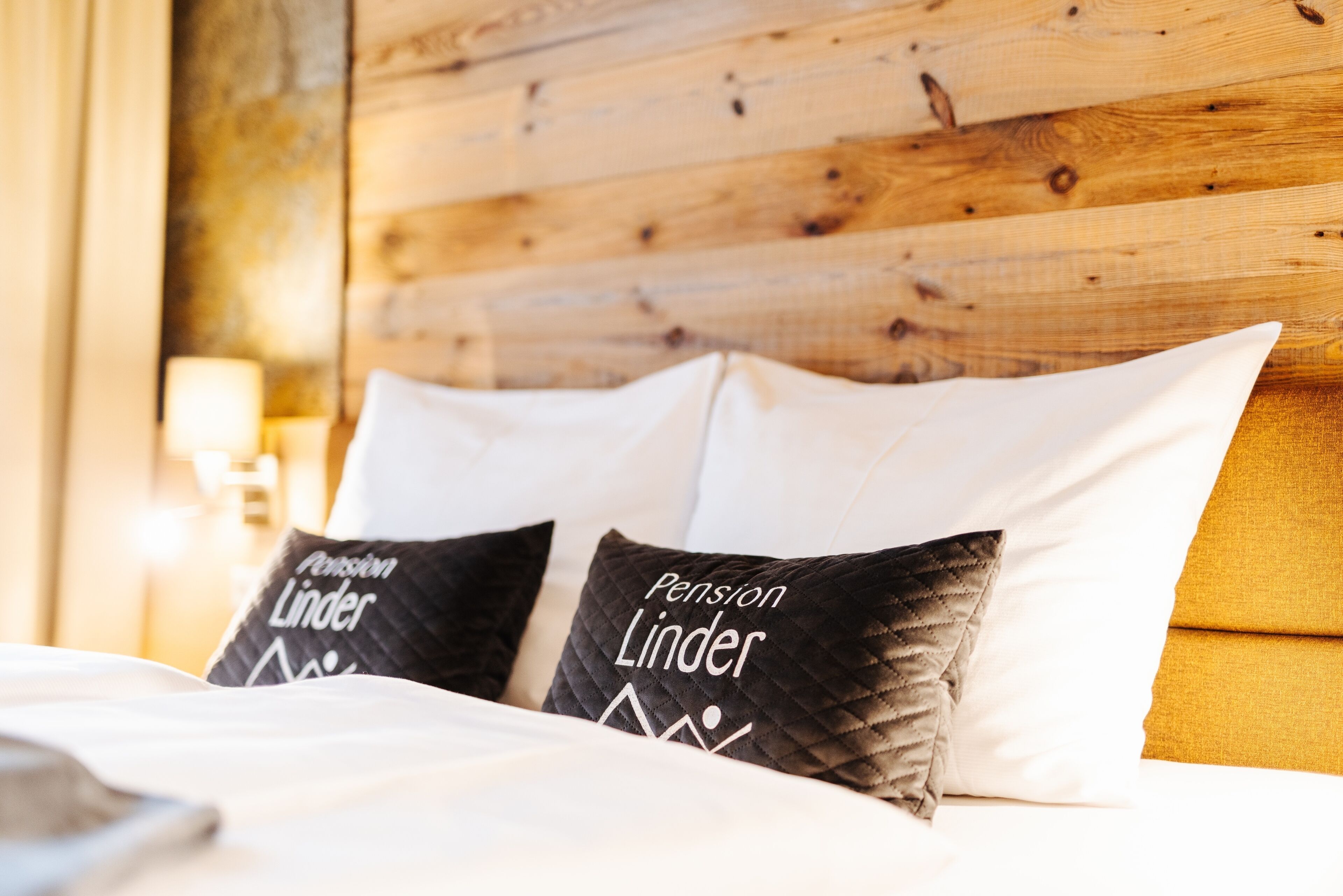 A bed with two pillows labeled "Pension Linder" and a wooden headboard.