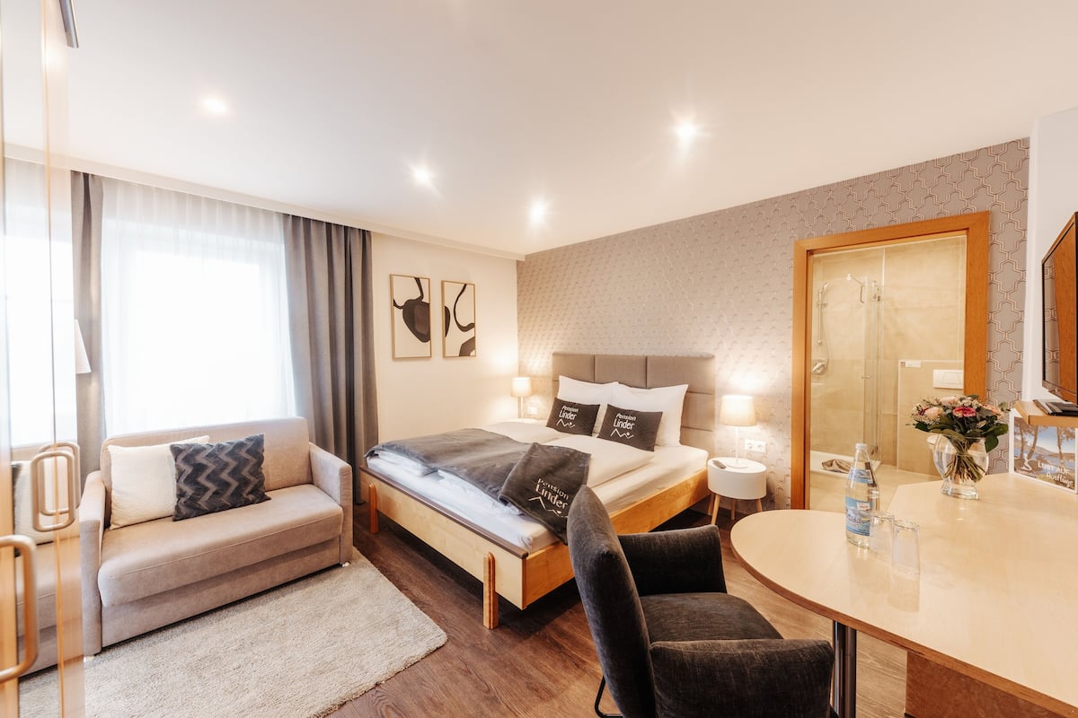 A modern hotel room with a bed, sofa, and dining area.