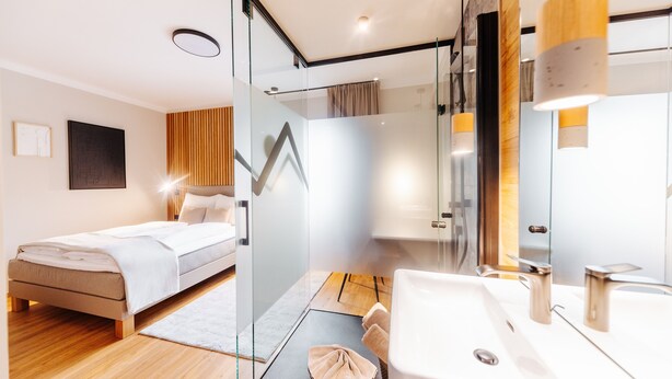 A modern bedroom with a bed, a glass shower enclosure, and a bathroom with a sink and mirror.