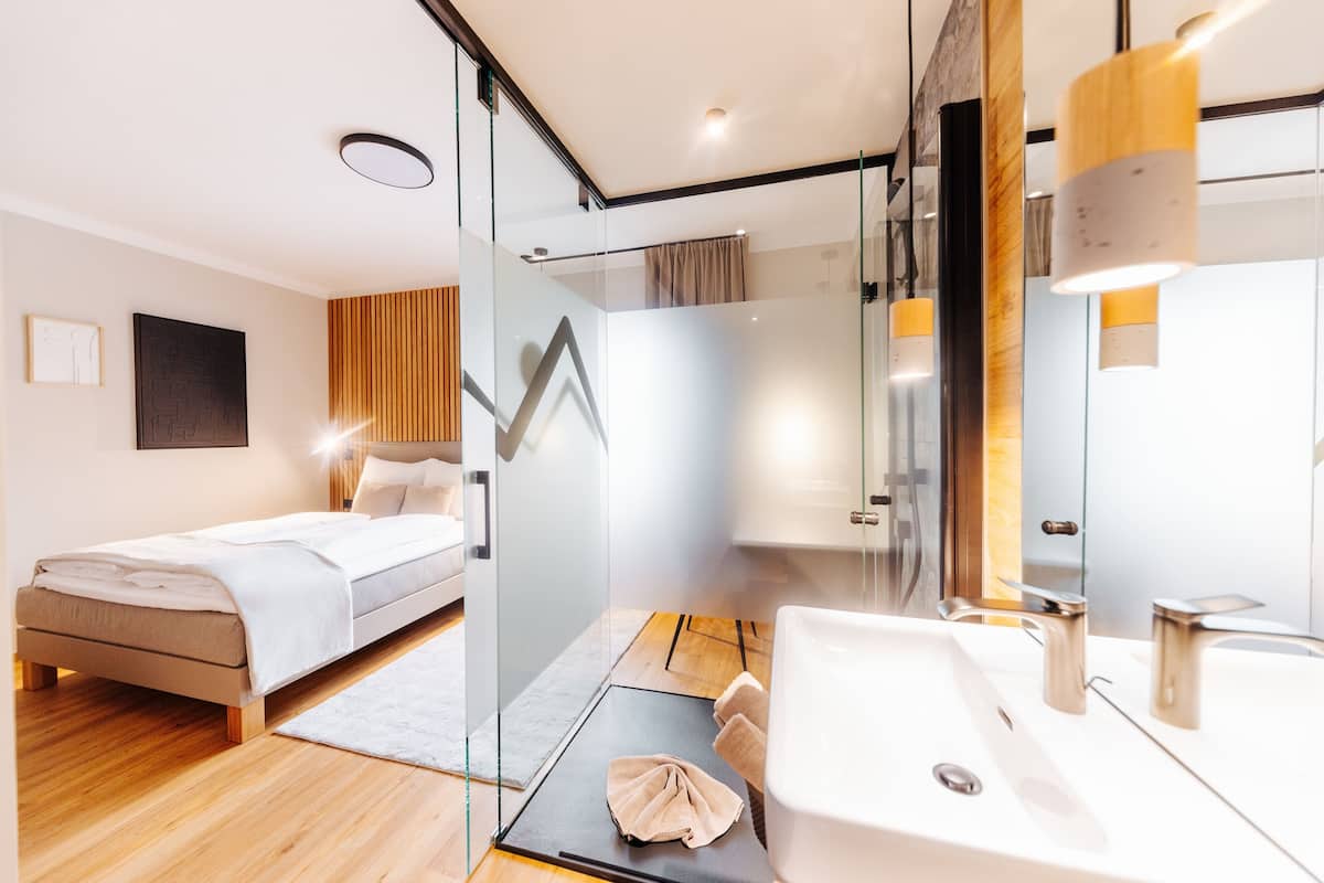A modern bedroom with a bed, a glass shower enclosure, and a bathroom with a sink and mirror.