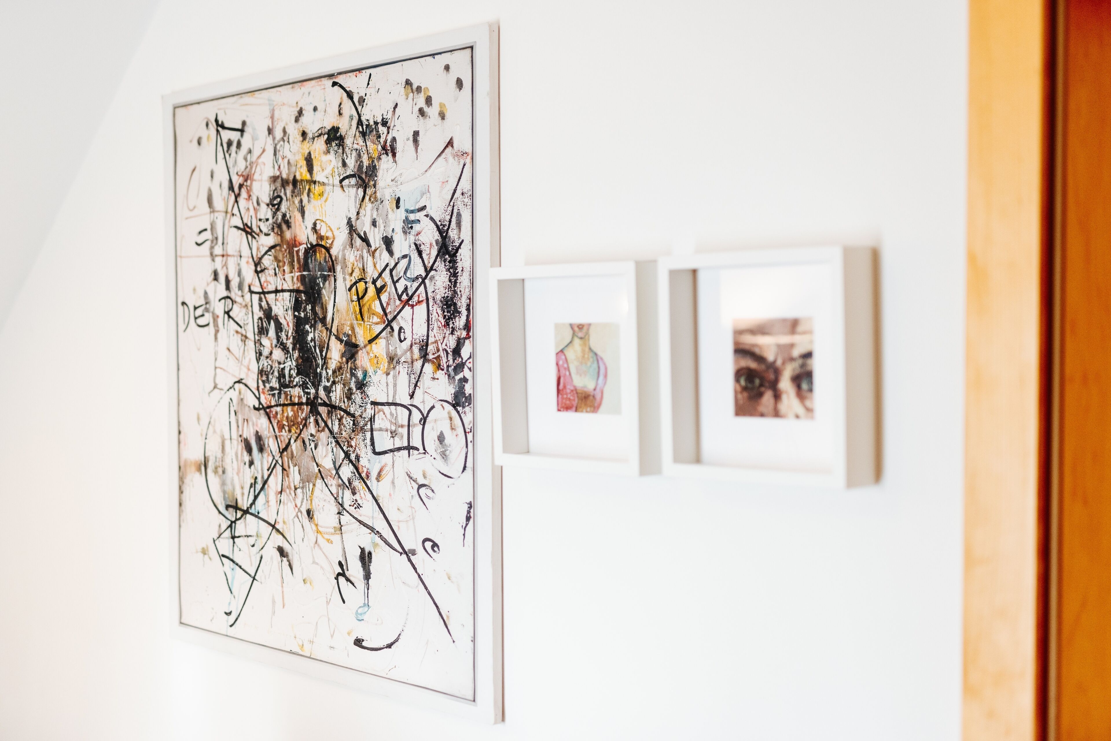 Una galería con una gran pintura abstracta y dos obras de arte más pequeñas enmarcadas en la pared.