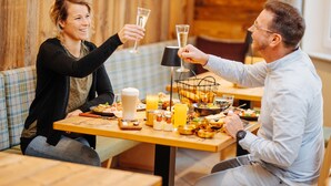 A dining area with a wooden table set for two, featuring a variety of dishes and drinks.