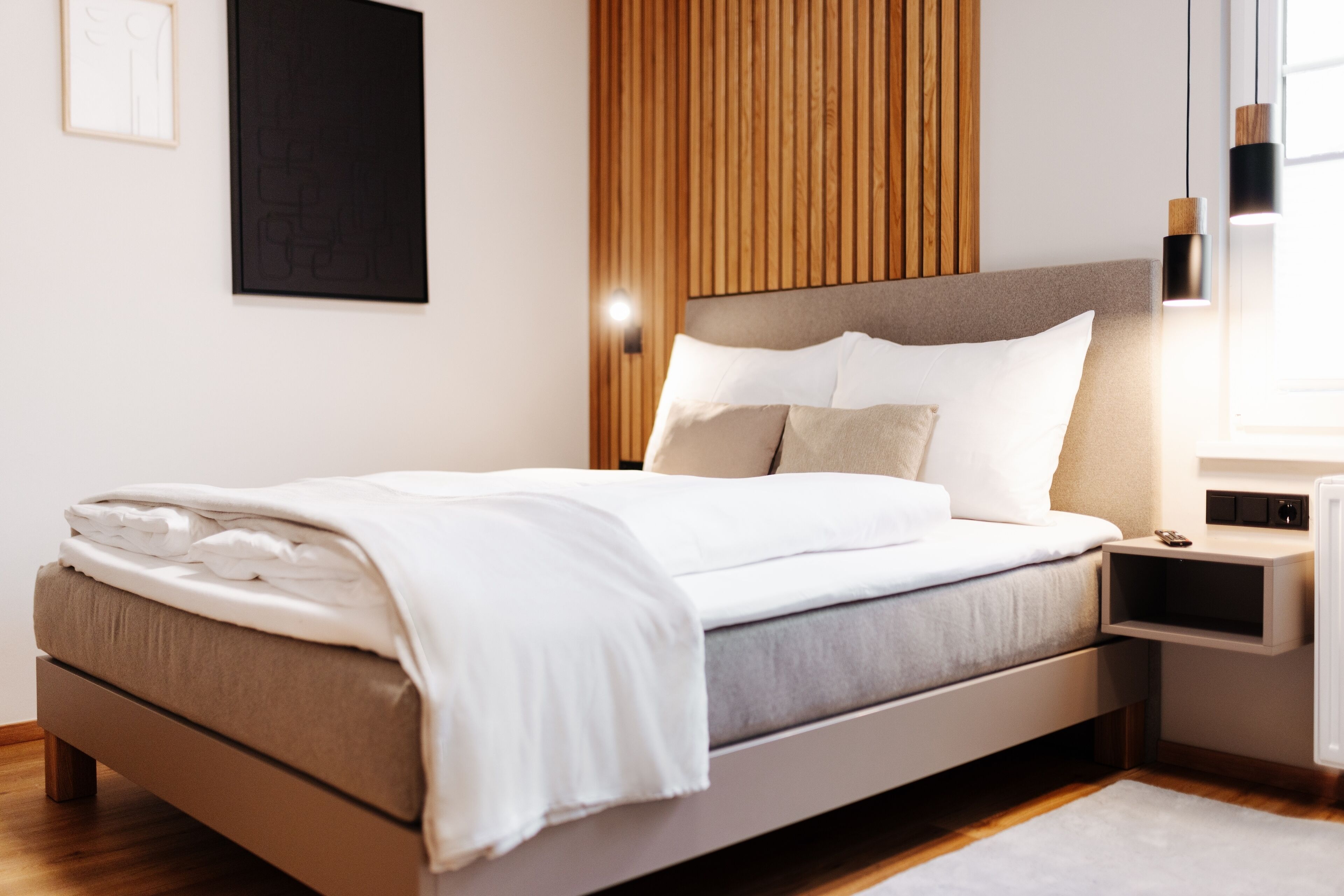 A modern bedroom with a bed, wooden panel wall, bedside table, and wall-mounted light.