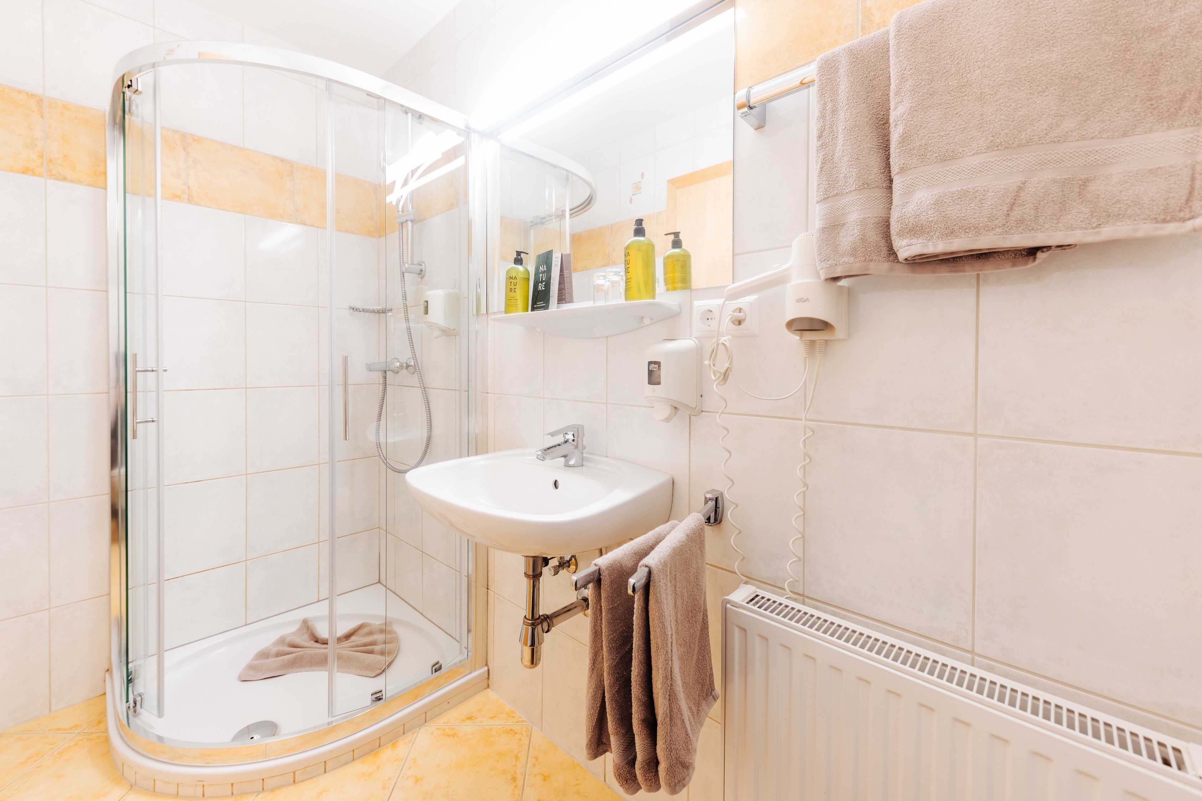 Une salle de bain avec une douche à parois de verre, un lavabo blanc et un porte-serviettes.