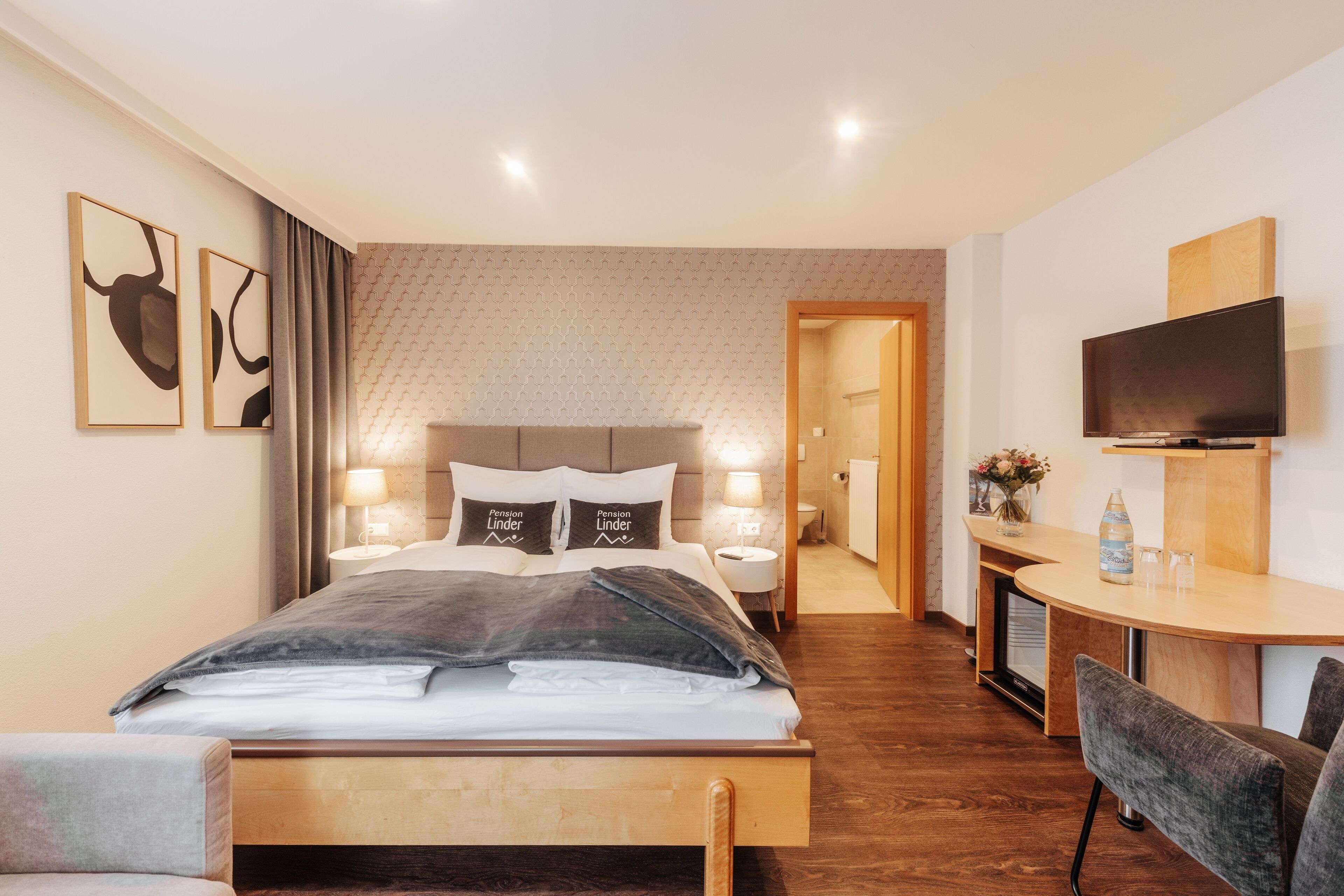 Una habitación de hotel moderna con una cama, lámparas de noche, un televisor, un escritorio y una silla.