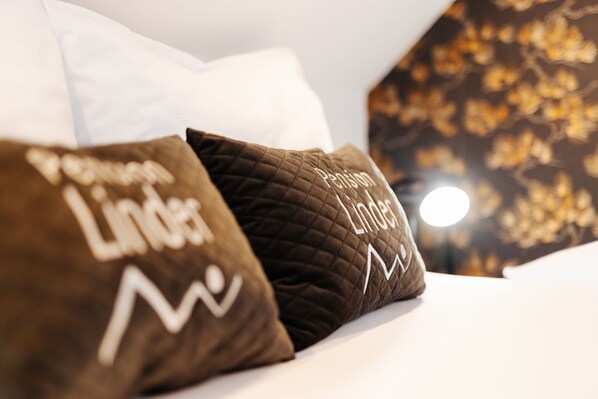 A bed with two pillows, one with 'Lindes' text and a quilted pattern, and another with 'Pension' text and a similar pattern.