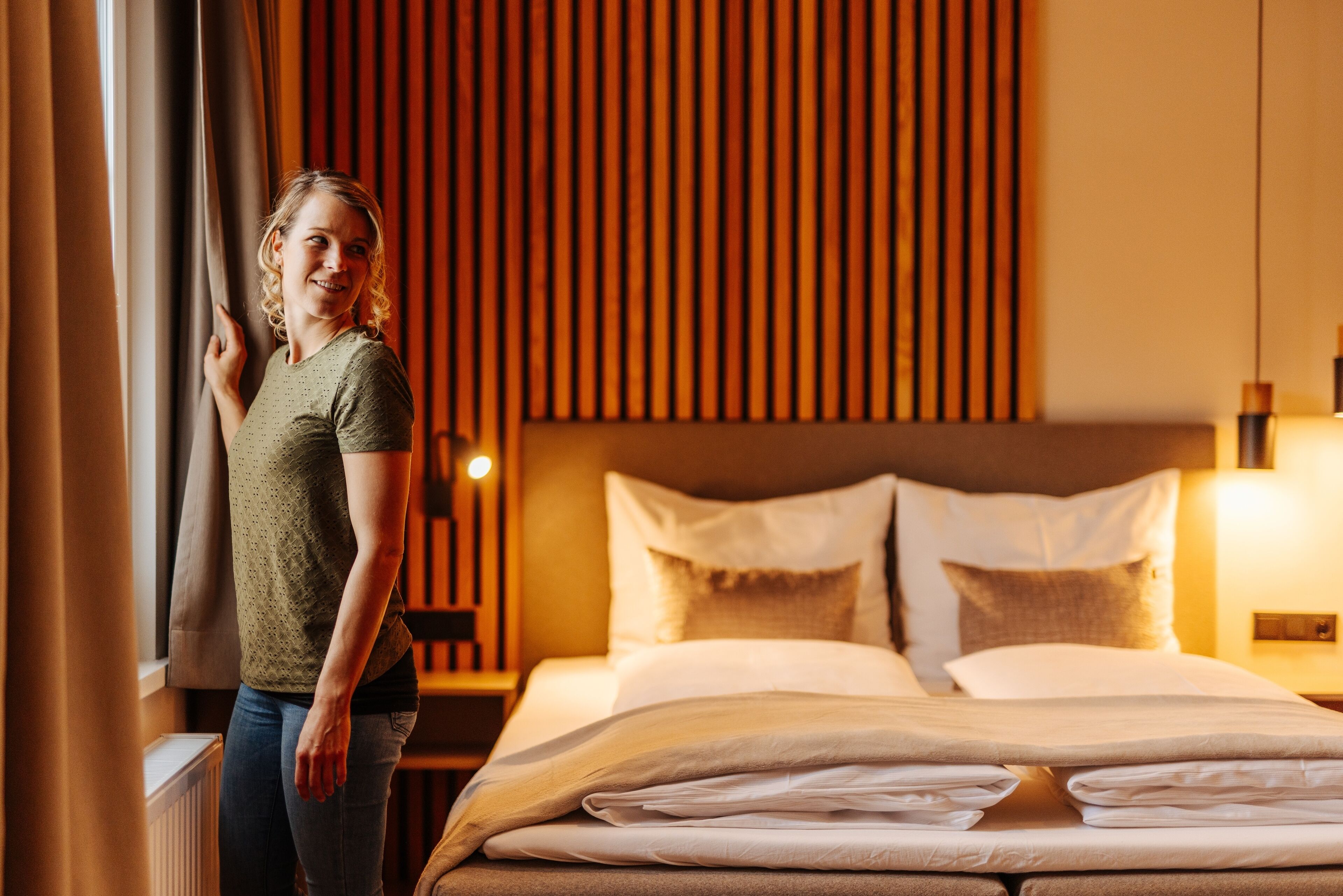 Ein Hotelzimmer mit Bett, Kissen, einem Nachttisch und einem Fenster mit Vorhängen.