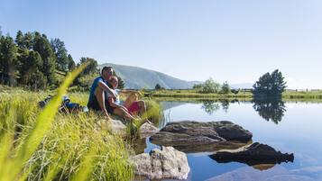 A couple sitting by a calm lake with mountains in the background.