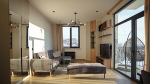 A modern living room with a sofa, ottoman, and TV, large windows with a city view, and a chandelier. - RIS Central Apartments Yerevan (Yerevan)