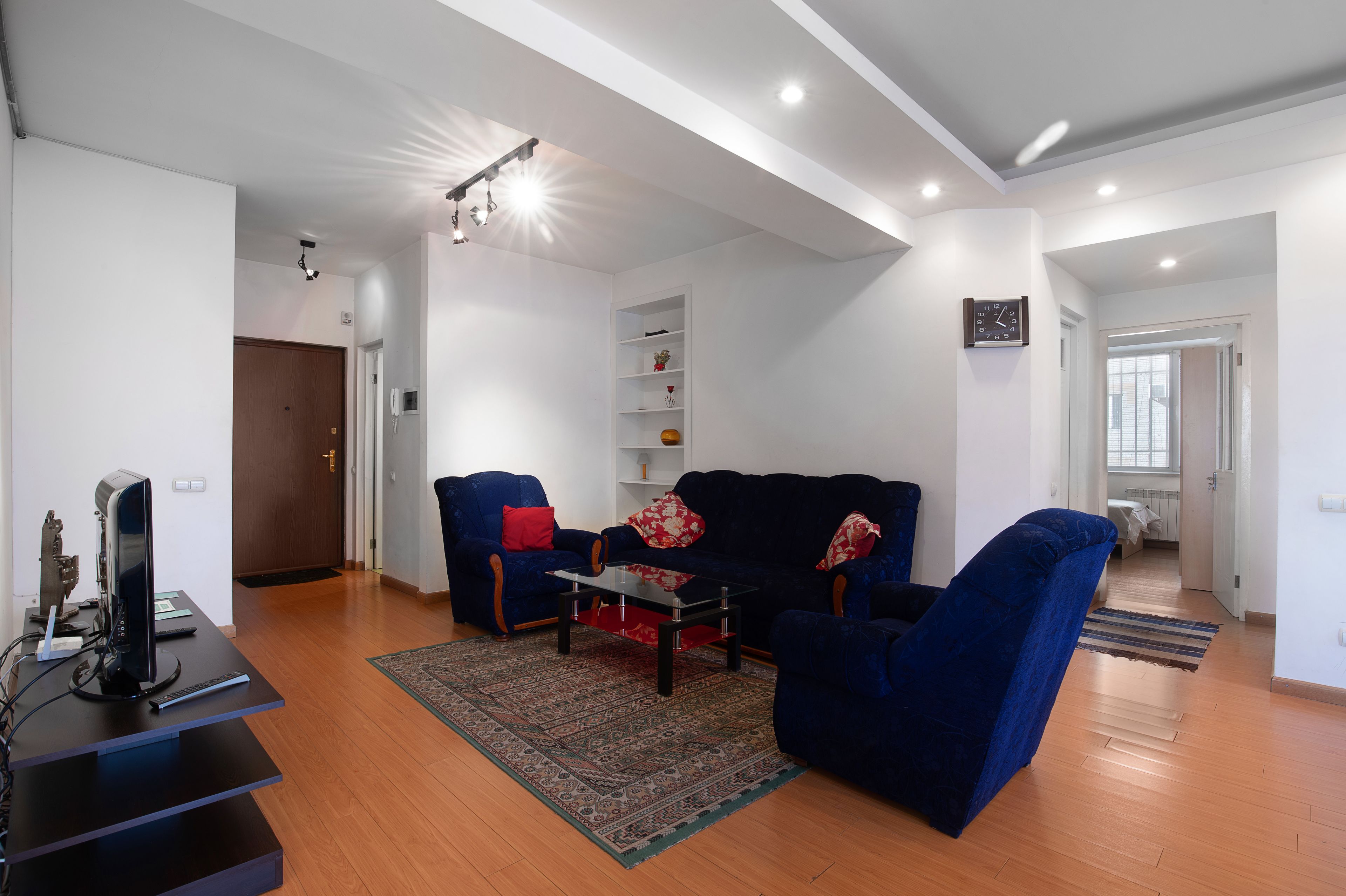 A modern living room with a blue sofa, a coffee table, and a TV on a stand. There is a wooden floor and a patterned rug.