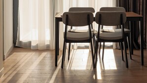 A room with a wooden floor, two chairs, a table, and a window with sheer curtains and a dark drape. - RIS Central Apartments Yerevan (Yerevan)