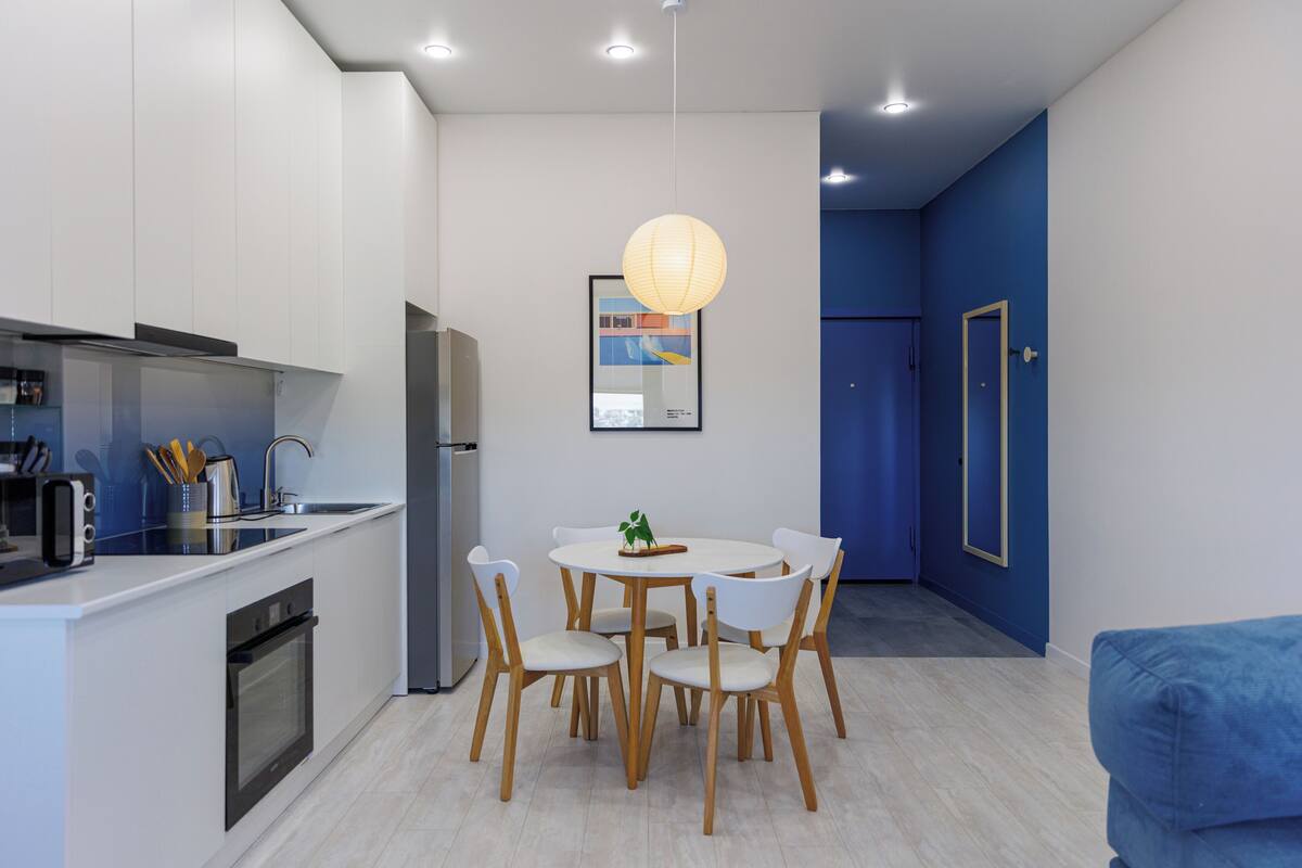 A modern kitchen with white cabinets, a built-in oven, and a dining area with a round table and chairs.