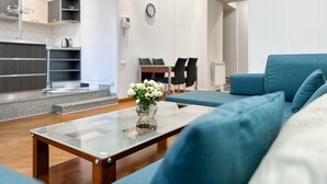 A modern living room with a glass coffee table, blue sofa, and a small white flower arrangement. - RIS Central Apartments Yerevan (Yerevan)