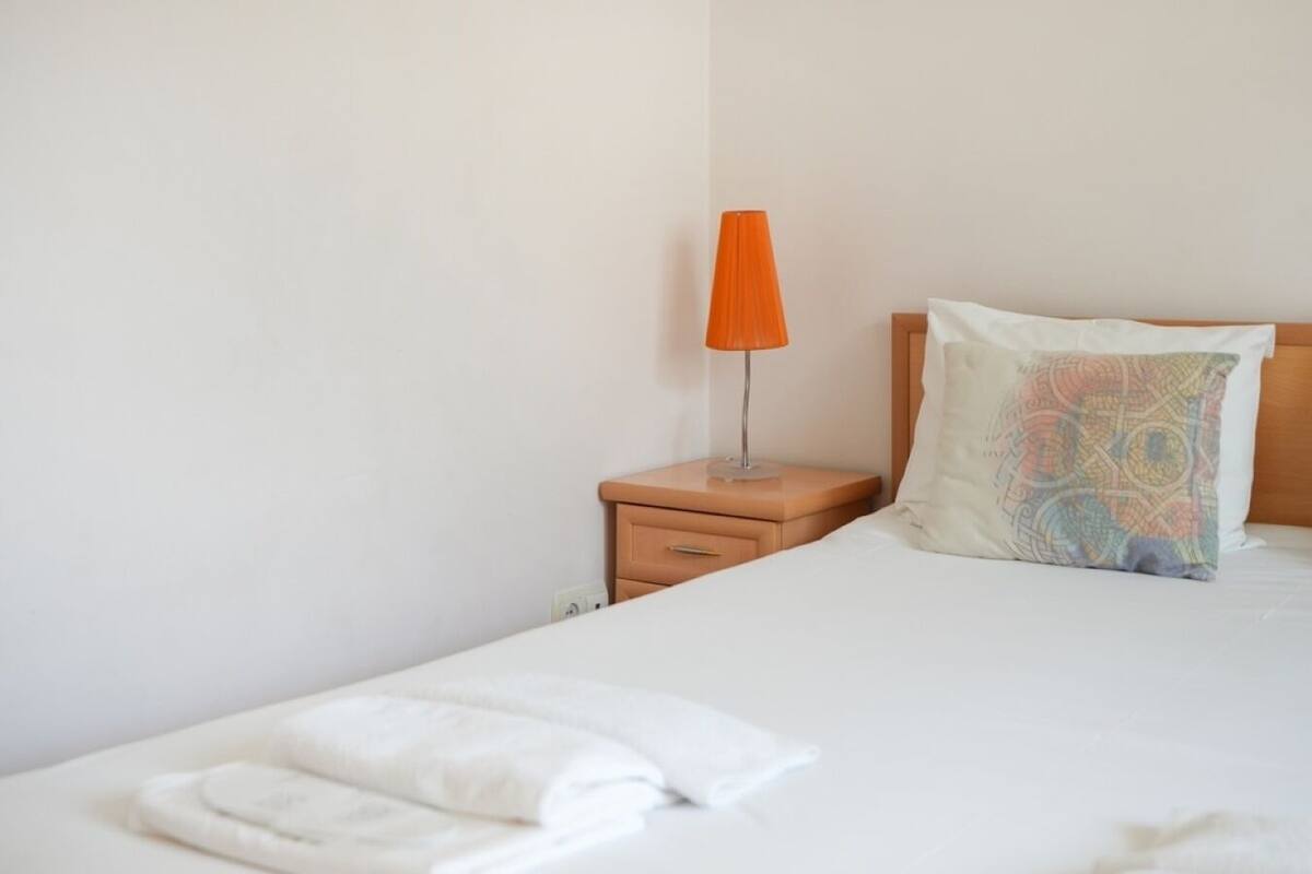 A neatly made bed with a white comforter and a folded white towel.
