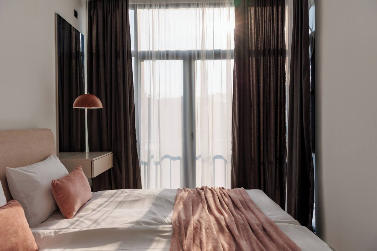 A neatly made bed with a blanket, a bedside lamp, and a nightstand with a mirror.
