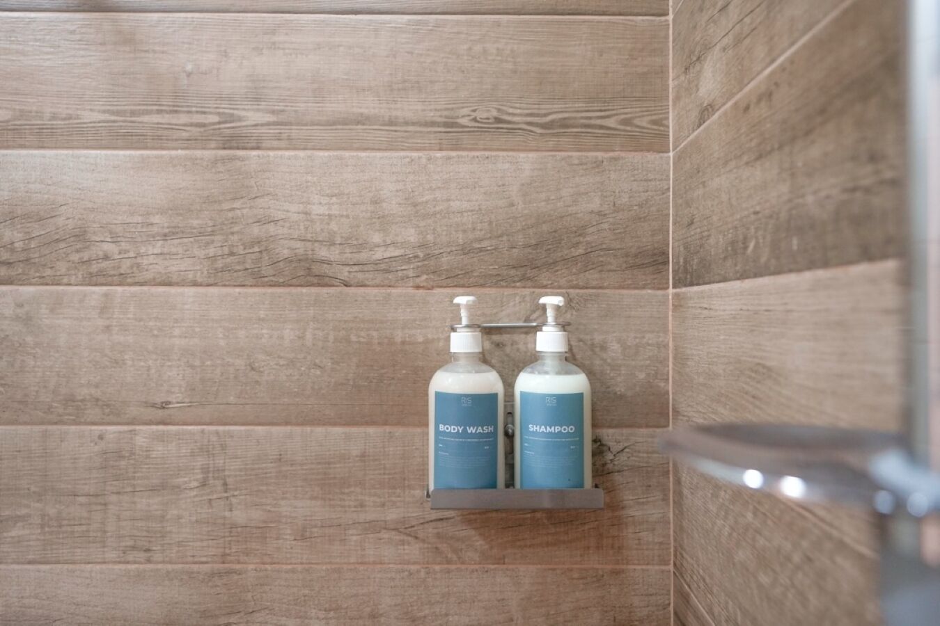 Douchegedeelte met houten lambrisering en twee flessen douche- en shampoo op een plank.