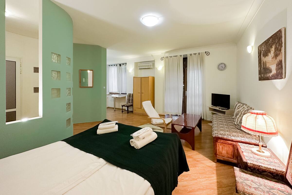 A hotel room with a bed, a desk, a chair, a sofa, a TV, and a lamp.