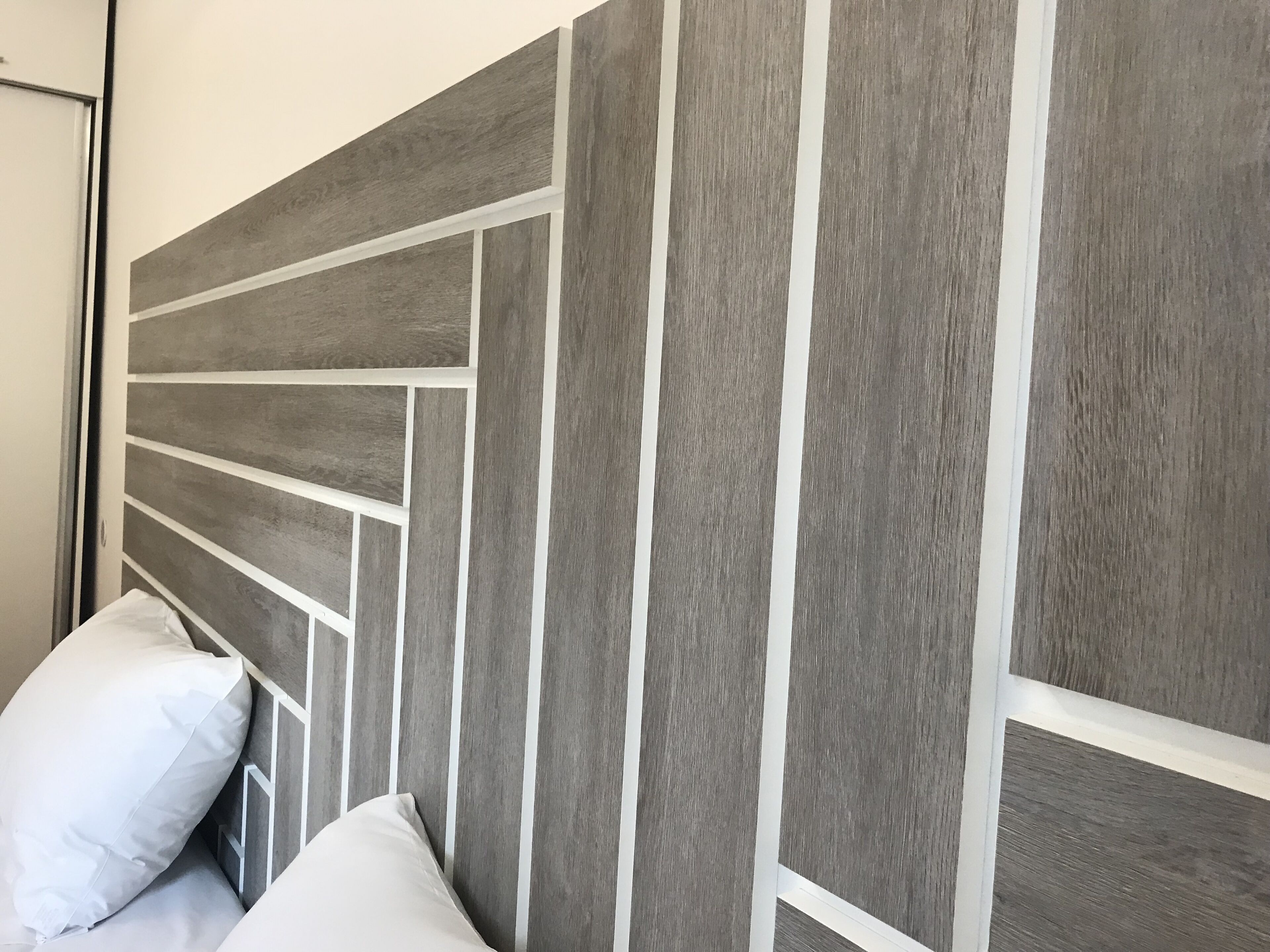 Une tête de lit ornée d’un motif géométrique et un coussin blanc.