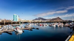 A marina with boats docked, a large industrial building, and mountains in the background. - Akranes Guesthouse (Akranes)