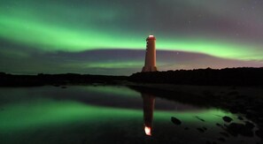 A lighthouse at night with the Northern Lights reflected in the water. - Akranes Guesthouse (Akranes)