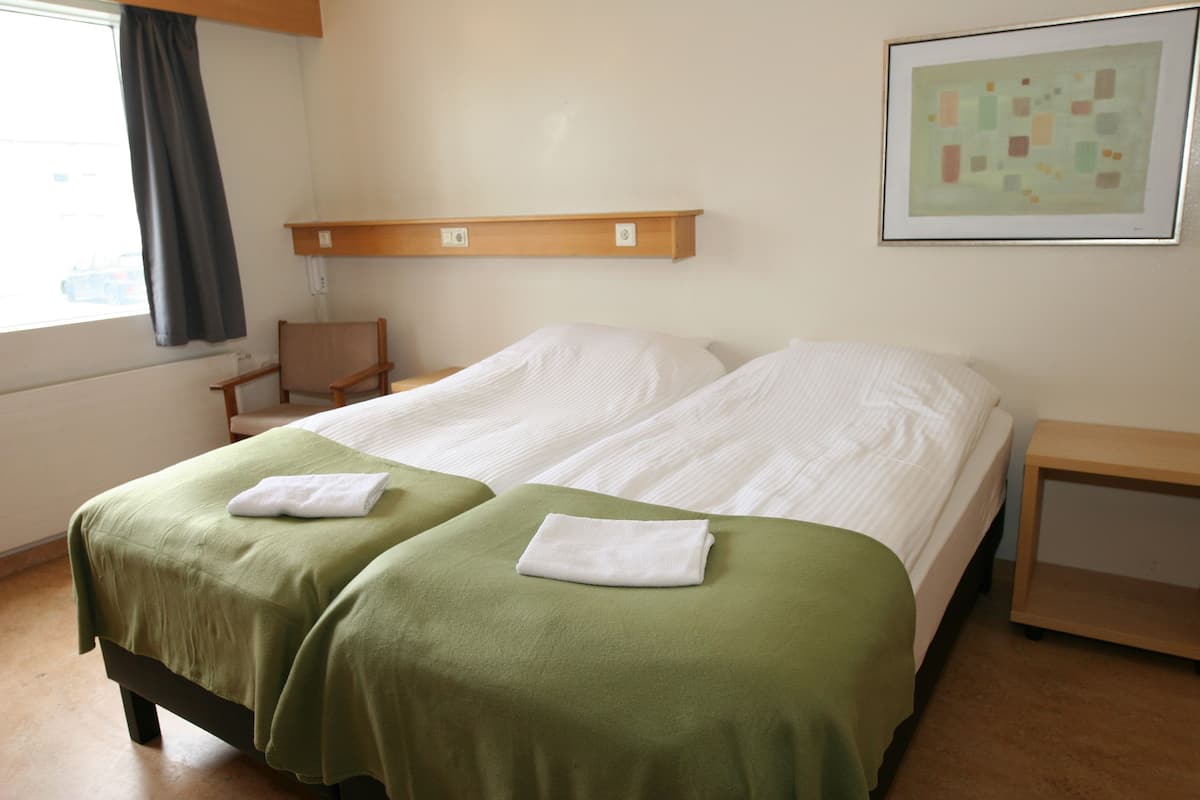 A hotel room with two beds, a wooden nightstand, a chair, and a framed picture on the wall.