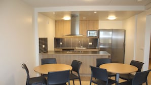 A modern kitchen with a microwave, refrigerator, and wooden cabinets. There are six black chairs around a wooden table. - Akranes Guesthouse (Akranes)