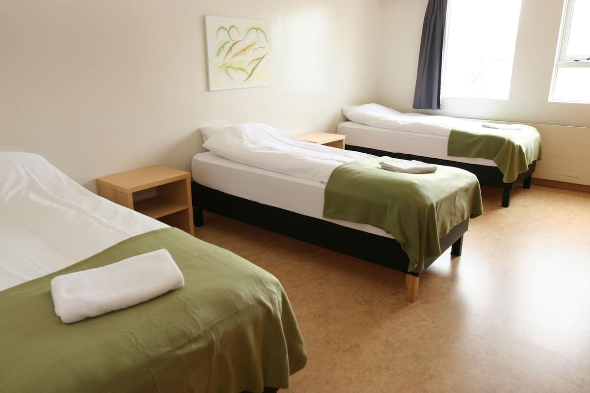 A room with three single beds, each with a wooden nightstand and a green bedspread.