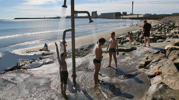 A beach with a water feature, rocky shoreline, and a distant industrial structure. - Akranes Guesthouse (Akranes)