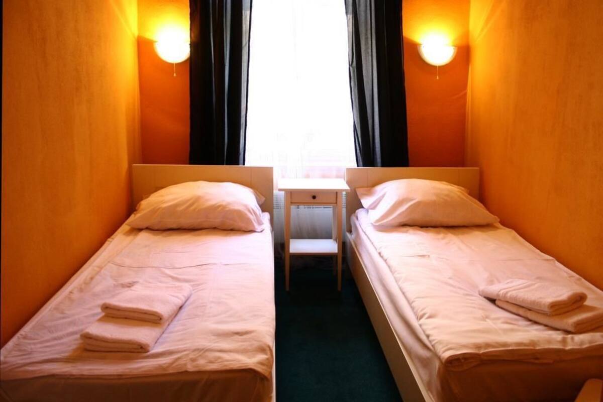 Una habitación con dos camas individuales, cada una con una almohada y una toalla doblada. Hay una pequeña mesa entre las camas.