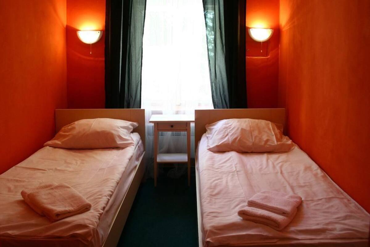 Dos camas individuales con almohadas y toallas dobladas, una mesita pequeña y una ventana con cortinas.
