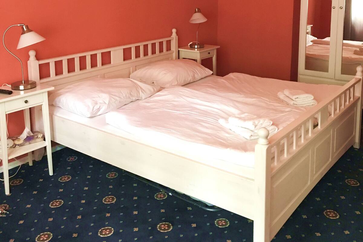 Habitación con una cama individual, dos mesitas de noche, un espejo y una alfombra estampada.