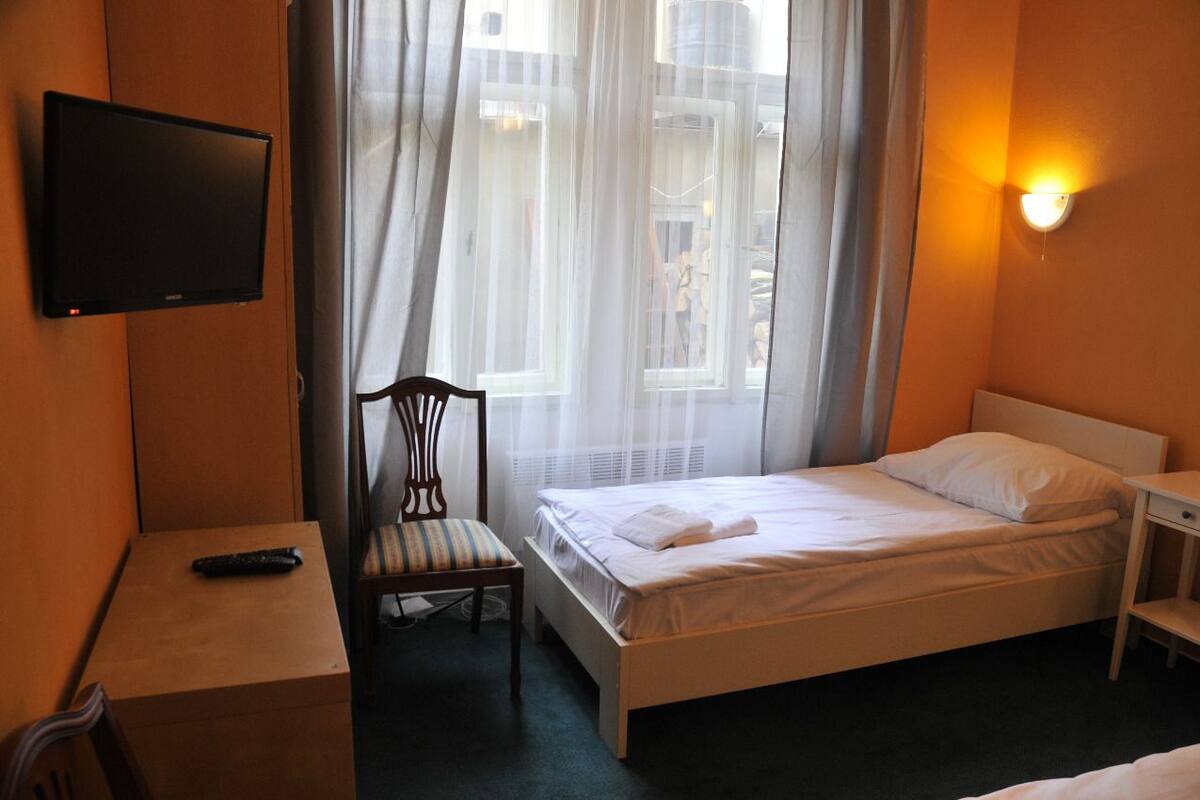 Habitación de hotel con cama, una silla, escritorio, televisor y ventana con cortinas.