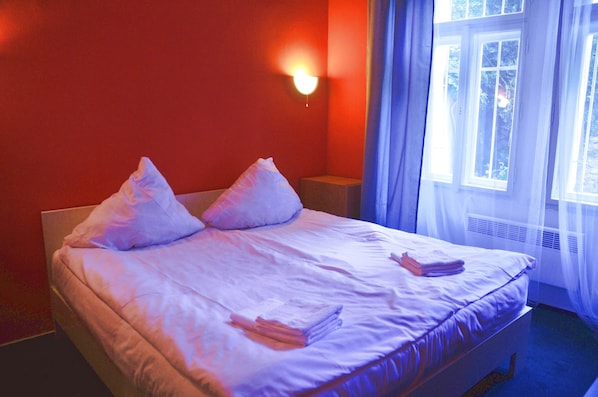 A bed with white linens and pillows, a bedside table, and a window with curtains.