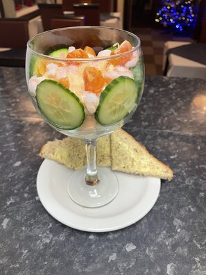 A dessert in a glass on a white plate, with cucumber slices and shrimp on top. - Ivydene Guest House (Skegness)