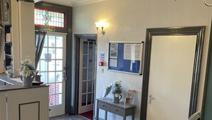 A reception area with a wooden floor, a reception desk, a bulletin board, a door with a sign, and a stained glass window. - Ivydene Guest House (Skegness)