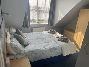 A bedroom with a bed, a dresser, a window with curtains, and a view of greenery outside. - Ivydene Guest House (Skegness)