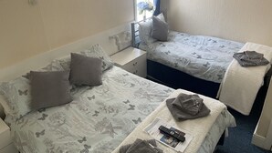 A hotel room with two single beds, each with a floral-patterned duvet and a pillow. There is a small table with a remote control and a folded towel. - Ivydene Guest House (Skegness)