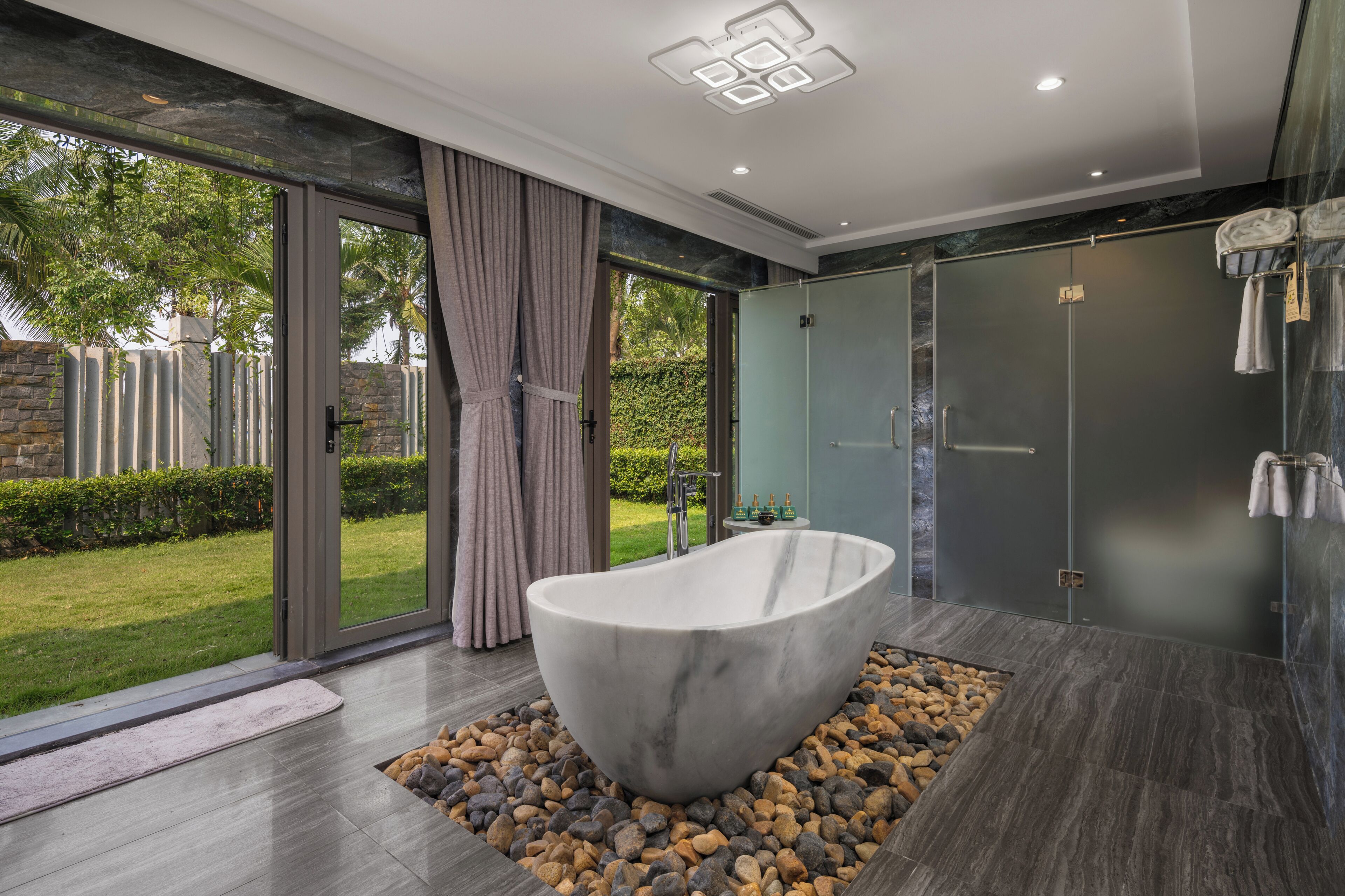 A modern bathroom with a freestanding bathtub, a glass shower enclosure, and a view of the outdoors.