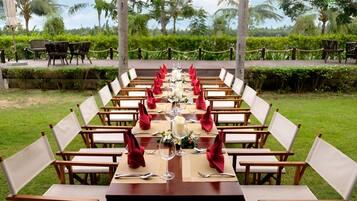 A long dining table set outdoors with white chairs and red napkins.