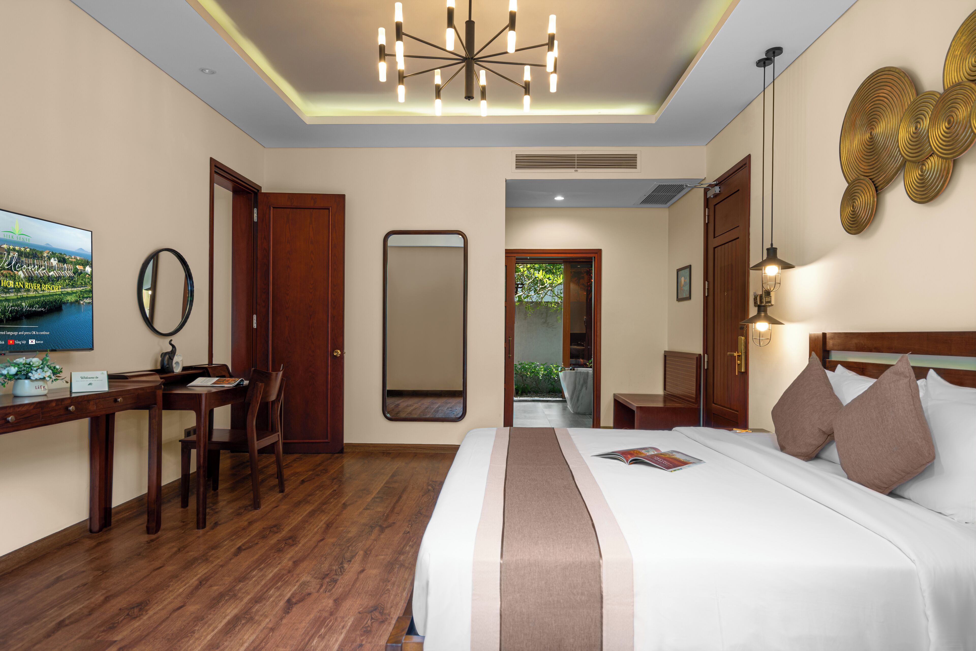 A hotel room with a large bed, a desk with a chair, a television, and a mirror.