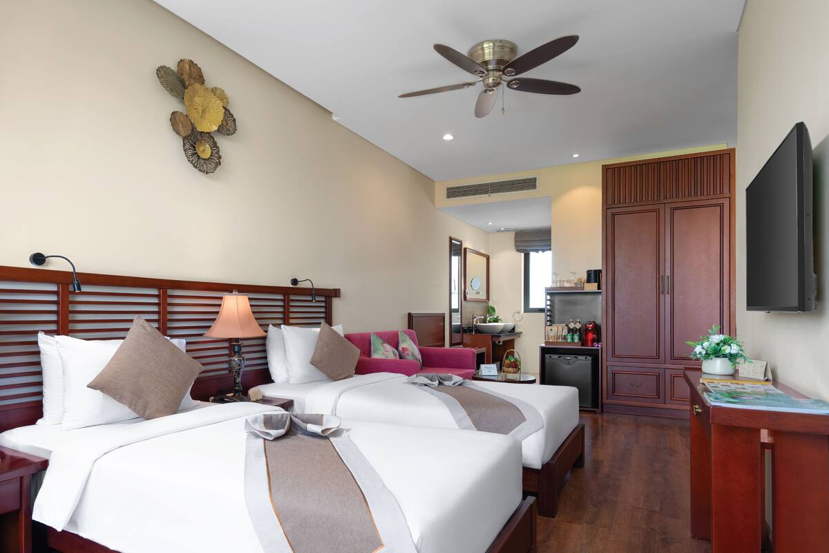 A hotel room with two beds, a ceiling fan, a TV, a desk, and a bathroom visible through an open door.