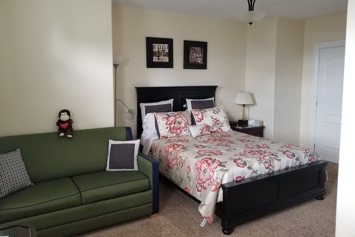 A bedroom with a bed, a green sofa, a nightstand, a lamp, and two framed pictures on the wall.