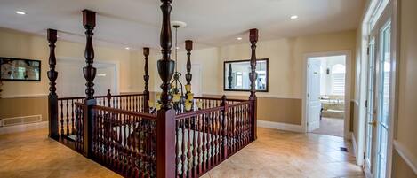 A spacious foyer with a central wooden railing, a tiled floor, and a large window on the right.