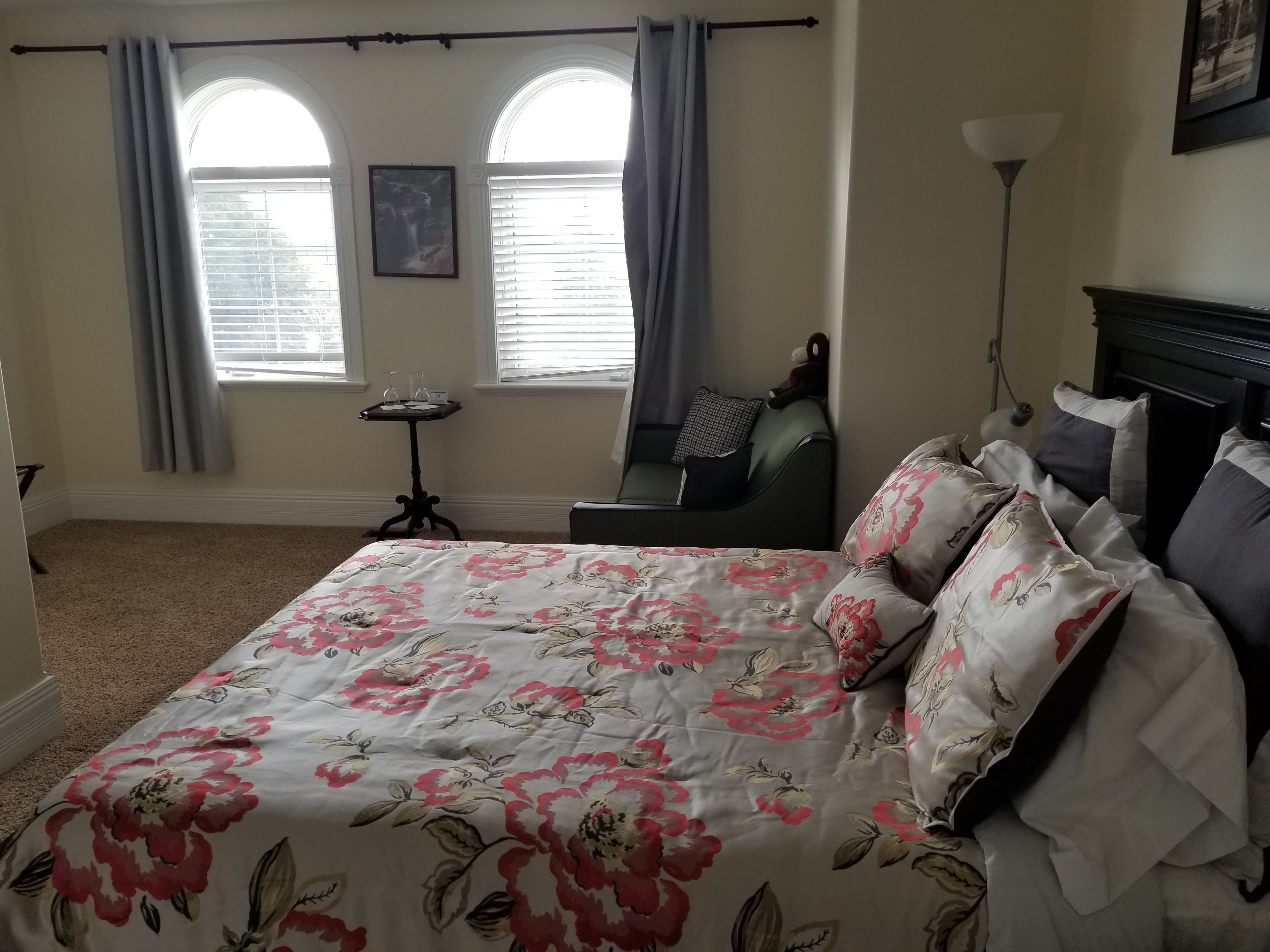 A bedroom with a floral bedspread, a chair, a small table with glasses, and a lamp.
