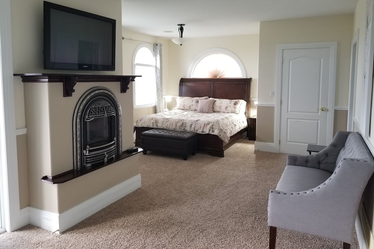 A bedroom with a fireplace, a bed, a television, and a chair.