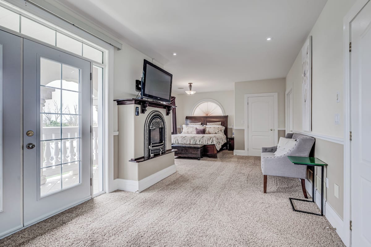 A bedroom with a fireplace, a bed, a TV, and a chair.