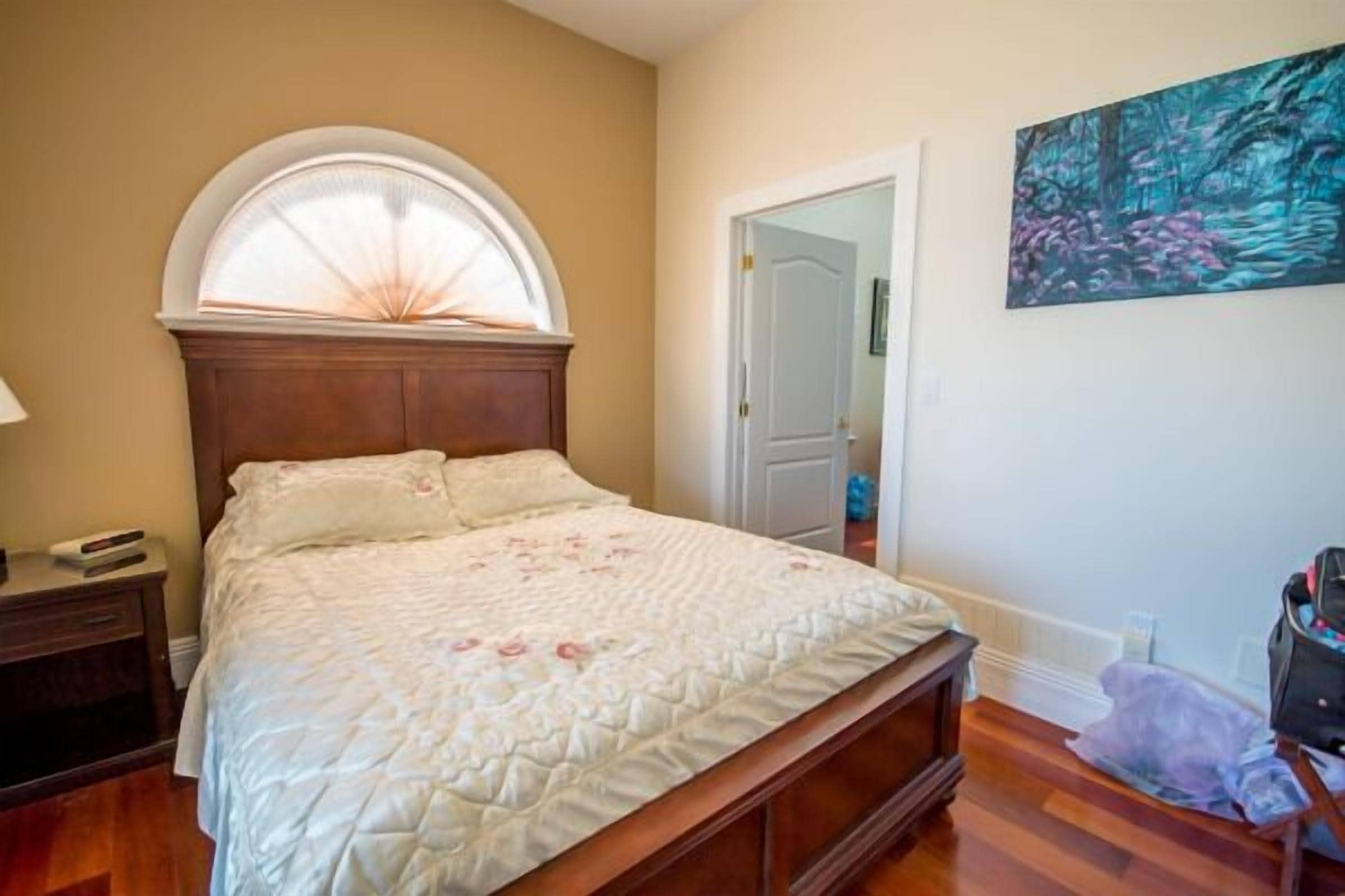 A bedroom with a wooden bed, a nightstand, a window with a white frame, and a painting on the wall.