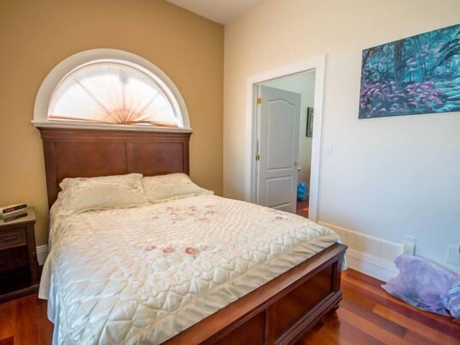 A bedroom with a wooden bed, a nightstand, a window with a white frame, and a painting on the wall.