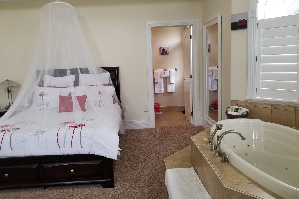 A bedroom with a bed under a canopy, a bathroom with a bathtub, and a hallway with towels.