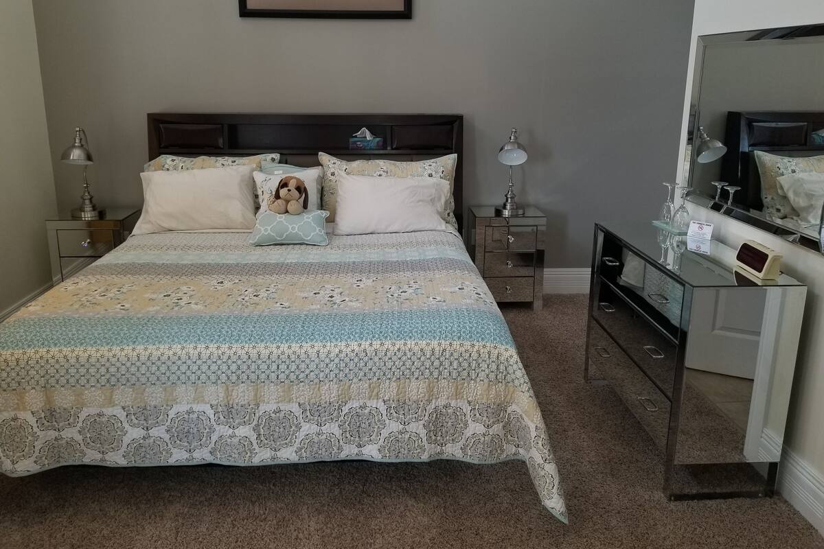 A neatly arranged bedroom with a large bed, two bedside tables, a dresser, and a mirror.